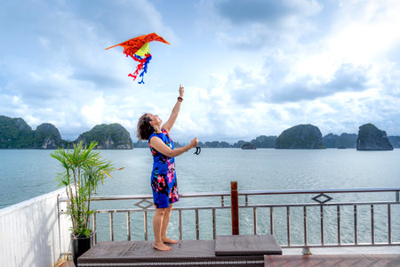 Ha Long Bay, Quang Ninh Province, Vietnam - July 3, 2020: Female tourist excited with colorful kite on the deck. Beautiful scenery of Ha Long Bay. North Vietnamのeditorial素材