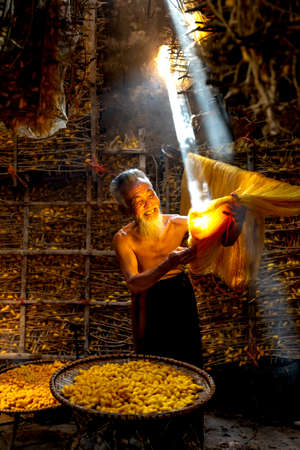 Vu Thu gold silk craft village, Thai Binh Province, VN - September 15, 2020: An old man is checking the quality of gold silk products in warehouse at Vu Thu gold silk craft village in Thai Binh, VNのeditorial素材