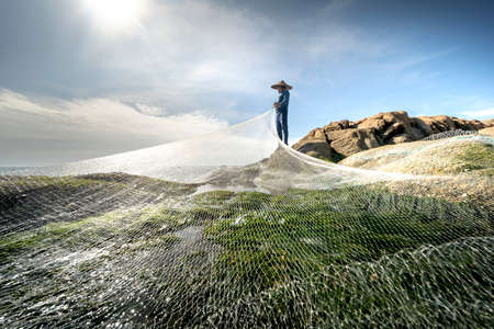 Ninh Thuan province, Vietnam - January 16, 2021: Fishermen throw nets to fish on a beach with lots of green mossのeditorial素材