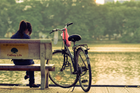 Hanoi, Vietnam - 28 August, 2011: The girl sits on the bench beside her bicycle at Hoan Kiem lakeのeditorial素材