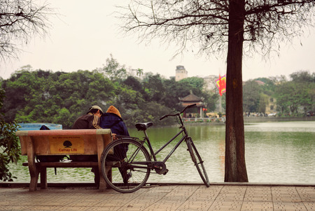 Hanoi, Vietnam - 10 March, 2012: The couple sit on the bench beside their bicycle at Hoan Kiem lakeのeditorial素材