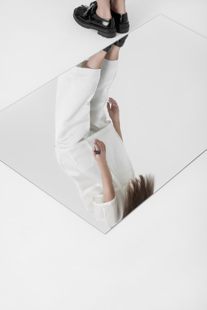 Crop shot of woman in white gown and black shoes bending back standing on white floor above mirror.の写真素材