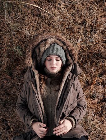 From above attractive young tourist in warm clothes sleeping on ground while resting in wild natureの写真素材