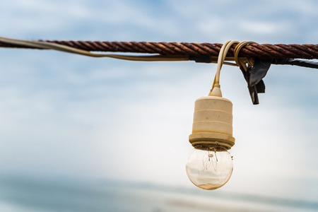 Close up of lamp string light hanging with rusty sling on blue sky background.の写真素材