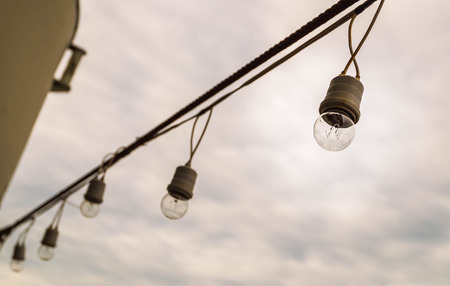Selective focus of lamp string light hanging with rusty sling on cloudy sky background.の写真素材