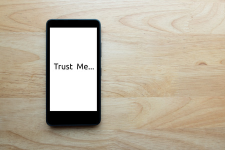 Smart phone show text on screen "trust me" status show today, human is the slave of technology too on wooden table background.の写真素材