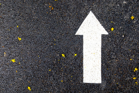 Close up of a white arrow sign on asphalt walking and running lane in the public park, selective...