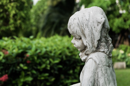 A white vintage little girl ceramic sculpture in the garden, selective focus.の写真素材