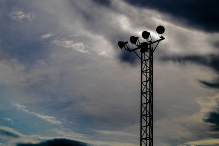 Silhouette of stand alone spotlight pole was closed with cloudy dark blue sky background, selective focus.の写真素材