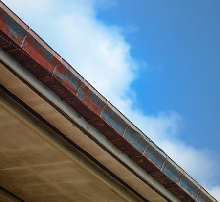 A broken roof gutter of the house on bottom view, old and rusty with blue sky background.