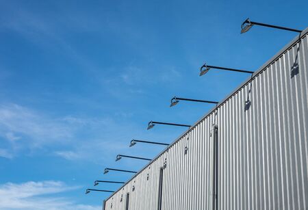 Street architecture outdoor lamp hanged and cantilevered from the wall of the building which is metal sheet with blue skyの写真素材