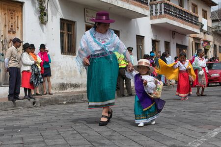 June 18, 2017 Pujili, Ecuador: indigenous kichwa woman walking on the street in colorful traditional dress at Corpus Christi parade holding a little girl by handのeditorial素材