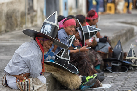 June 24, 2017 Cotacachi, Ecuador: indigenous kichwa men sitting on the sidewalk tired after  participating in a parade at summer solsticeのeditorial素材