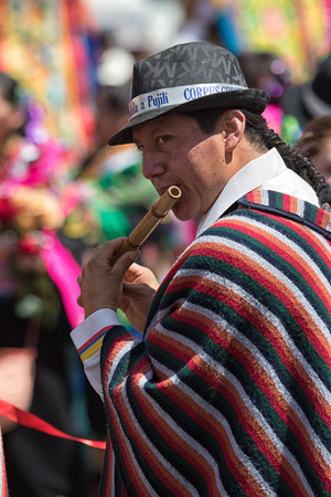 June 17, 2017 Pujili, Ecuador: man wearing traditional poncho playing a bamboo flute at Corpus Christi paradeのeditorial素材