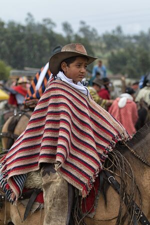 June 10, 2017 Toacazo, Ecuador: young kichwa boy wearing a poncho on horseback in the rain at a rural rodeoのeditorial素材