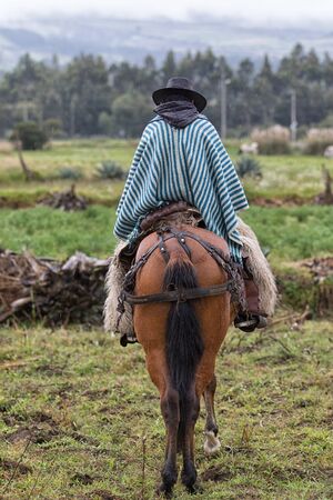 June 10, 2017 Toacazo, Ecuador: lonely cowboy on horseback wearing a traditional poncho on a rainy dayの写真素材