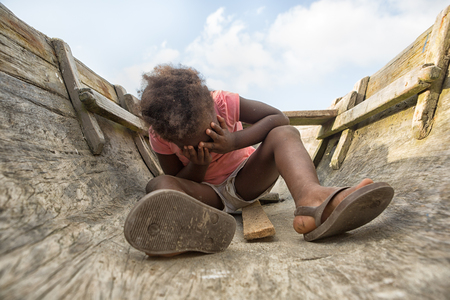 Sambo Creek, Honduras: a young garifuna girl sitting on the bottom of a dugout canoe with her palms over her faceの写真素材