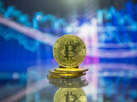 Golden bitcoin are stacked on a bright background of business graphs close-up. Bitcoin...
