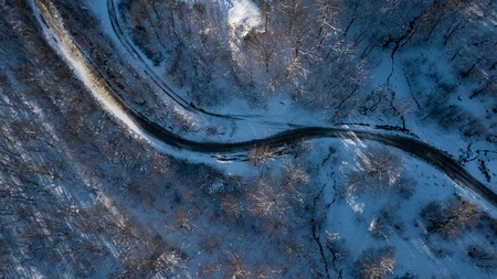 Curvy windy road in snow covered forest, top down aerial view.の写真素材