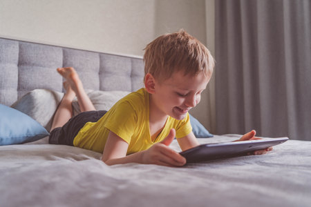 Distance education, learning. Boy is lying on the bed with a tablet in the room. Child with a...