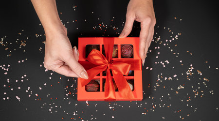 Various handmade chocolate truffle candies in a red box on a dark background in female hands.