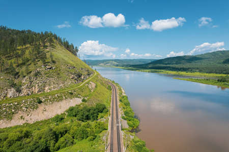 Flying above a glacial river in Siberia, Russia with green mountains and railway track in the background.の写真素材