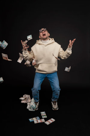 Young happy businessman dancing with a stack of money isolated on black background.