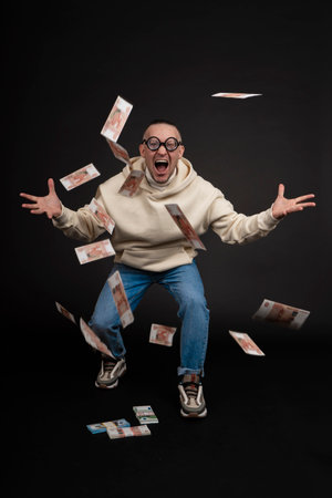 Young happy businessman dancing with a stack of money isolated on black background.の写真素材