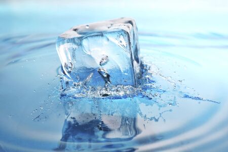 cool refreshing ice-cube dropped into freshly poured water. splashes frozen in time.の写真素材