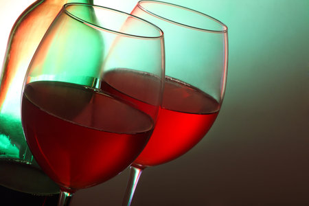 two glasses of red wine with bottle, backlit with coloured filtersの写真素材