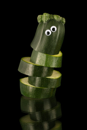 Slices of courgette/ zucchini , arranged in an animated style.Eyes applied to create appealing character, isolated on a black background on a reflective surface.の写真素材