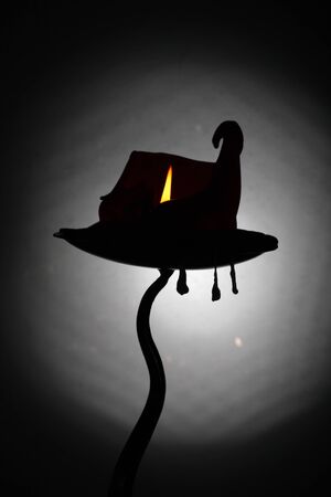 A gnarled curling burning candle that resembles a witches hat / haunted house ,with three wax pendant drips suspended from the candle holder.の写真素材