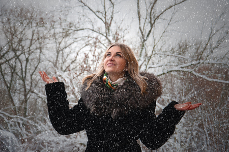 Beautiful happy smiling woman in winter outdoors. In the street snowfall. The girl lifted her hands...