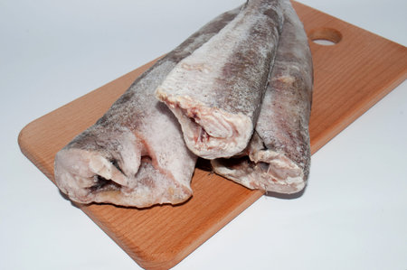 Frozen fish hake close-up on a wooden cutting board on a white background, close-up