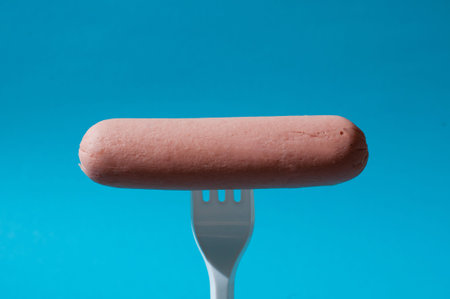 Raw sausage on blue background with a plastic forkの写真素材