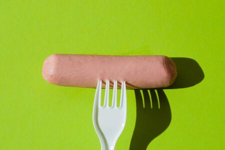 Sausage and plastic fork on green backgroundの写真素材