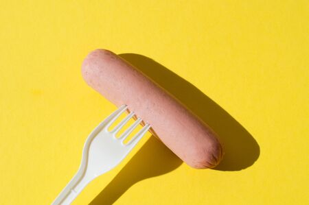Sausage and white plastic fork on bright yellow background with hard lightの写真素材