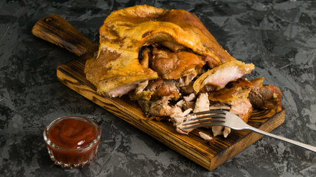 Pork knuckle baked in the oven with chicken. Various baked meats on a wooden cutting board and tomato sauce on a dark background, rustic style.の写真素材