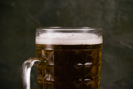 Delicious light beer in a beer mug on a dark background, white beer foam close-up.の写真素材