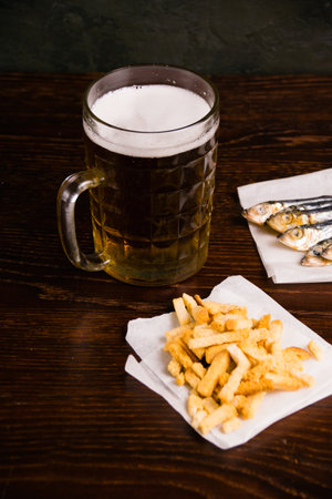 Delicious light beer in a beer mug, crackers and dried fish on a dark background.の写真素材