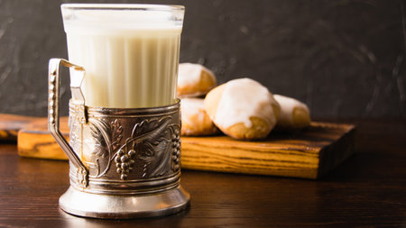 Glass of hot milk and delicious homemade gingerbread cookies with honey and cinnamon on dark wooden background with copy space.の写真素材