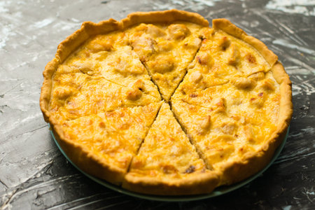 Delicious French quiche pie with chicken and cheese cut into pieces, on a dark background with place...