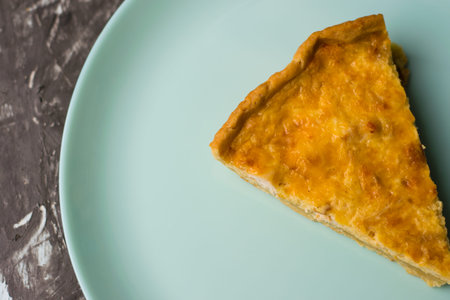 Flatlay, a piece of delicious open quiche pie with chicken, cheese and cream on a turquoise plate....