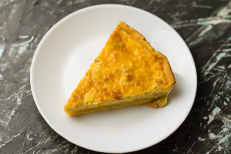 Flatlay, a piece of delicious open-faced quiche pie with chicken, cheese and cream on a white plate....