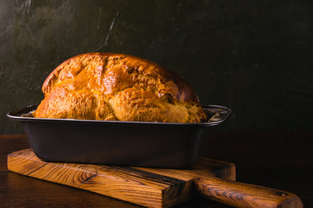 Sweet brioche bun in a bread baking pan, on a dark background. Delicious homemade pastries.