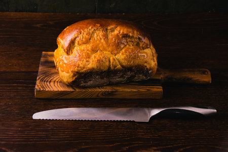 Sweet brioche bun on a wooden cutting board and a bread knife. Delicious home baked goodsの写真素材