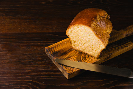 Sweet brioche bun cut on a wooden cutting board and bread knife. Delicious home baked goods.の写真素材