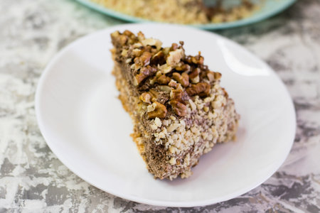 Delicious homemade cake with meringue, peanuts and walnuts on a light background. Appetizing piece of cake on a white plate close-up. Concept of natural homemade baking.の写真素材