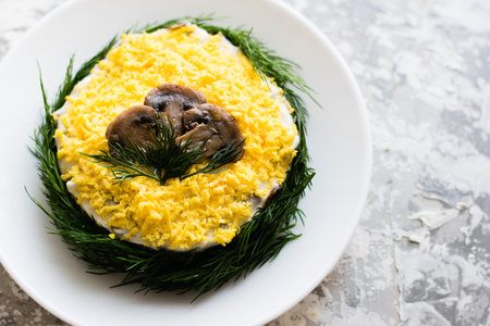 Delicious holiday salad with champignon mushrooms, eggs, canned green peas, mayonnaise and dill on a white plate on a light background with copy space.の写真素材