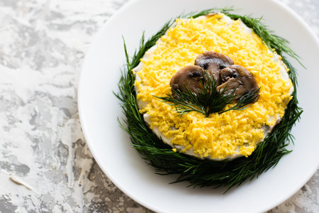 Delicious holiday salad with champignon mushrooms, eggs, canned green peas, mayonnaise and dill on a white plate on a light background with copy space.の写真素材